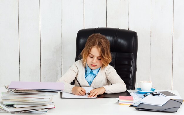 Junges hübsches Mädchen, das am Arbeitsplatz sitzt und im Büro schreibt.