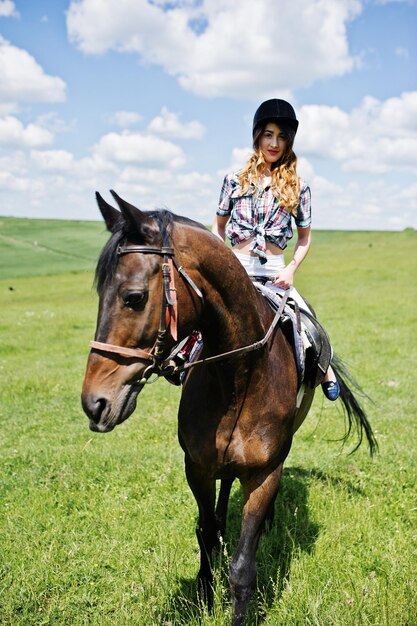 Junges hübsches Mädchen, das an einem sonnigen Tag auf einem Feld reitet