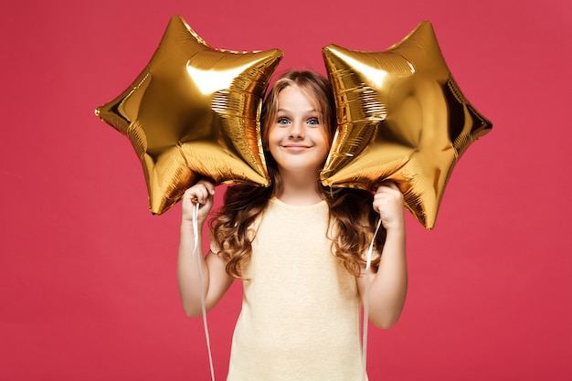 Junges hübsches Mädchen, das Ballons hält und über rosa Wand lächelt