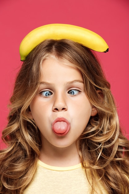 Kostenloses Foto junges hübsches mädchen, das banane auf kopf über rosa wand hält