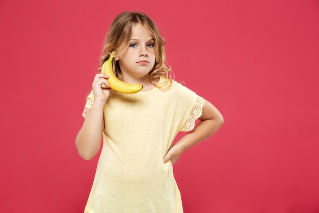 Junges hübsches Mädchen, das Banane wie Telefon über rosa Wand hält