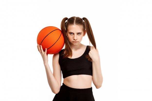 Junges hübsches Mädchen, das mit Basketball aufwirft, lokalisiert auf weißer Wand