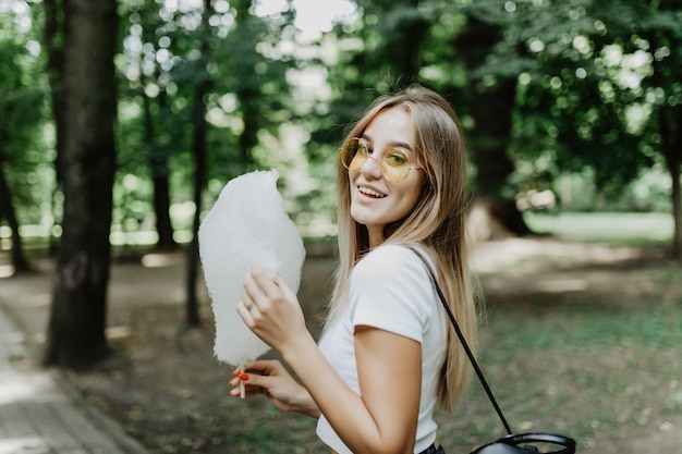 Junges hübsches Mädchen, das Zuckerwatte im Park isst