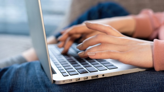 Junges Inhaltsschöpfermädchen sitzt auf ihrem Laptop auf dem Sofa. Arbeiten mit Fotos von zu Hause aus