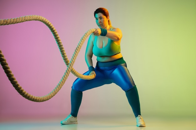 Junges kaukasisches plus size weibliches Model Training auf lila grüner Wand mit Farbverlauf im Neonlicht.