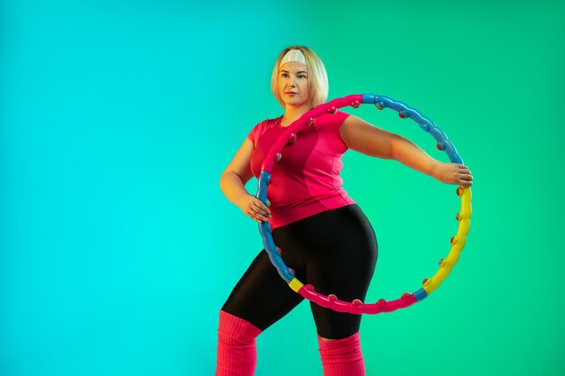 Junges kaukasisches plus size weibliches Modell Training auf grünem Hintergrund der Steigung im Neonlicht.