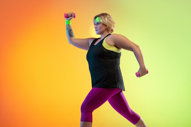 Junges kaukasisches plus size weibliches Modell Training auf orangefarbenem Hintergrund der Steigung im Neonlicht.