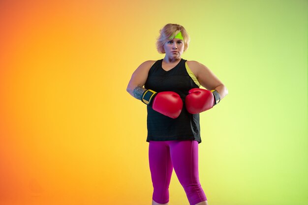 Junges kaukasisches plus size weibliches Modell Training auf orangefarbenem Hintergrund der Steigung im Neonlicht.