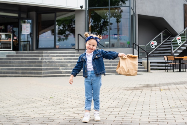 Junges kleines Mädchen mit Fast-Food-Tasche in der Nähe von Café im Freien