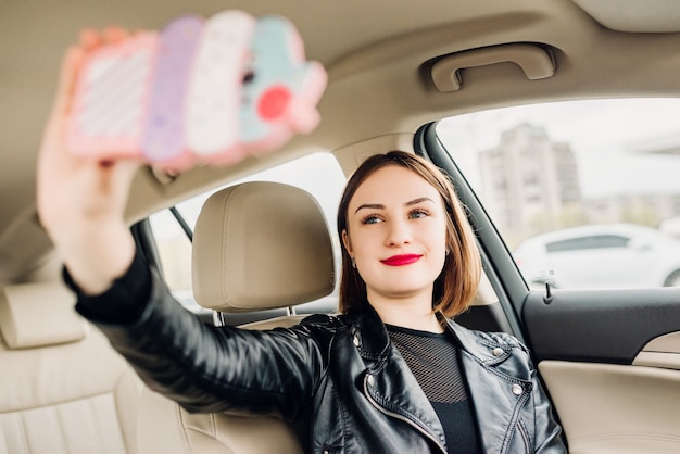 Junges lächelndes gril, das das selfie Porträt sitzt im Auto macht