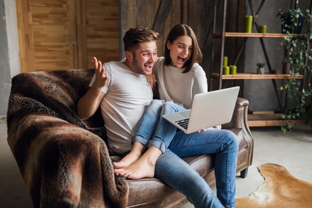 Junges lächelndes Paar, das auf Couch zu Hause im lässigen Outfit sitzt