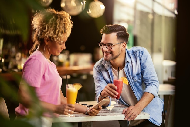 Junges lächelndes Paar, das sich in einem Café entspannt und Fruchtcocktails trinkt Frau ist Textnachrichten auf dem Handy