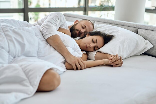 Junges Liebespaar, das umarmt liegt, während es auf einem Bett schläft