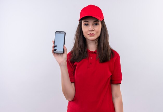 Junges Liefermädchen, das rotes T-Shirt in der roten Kappe hält, die ein Telefon auf lokalisiertem weißem Hintergrund hält