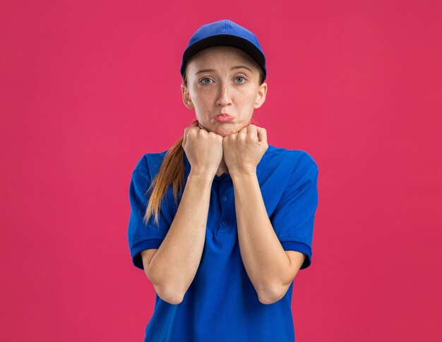 Junges Liefermädchen in blauer Uniform und Mütze mit traurigem Gesichtsausdruck