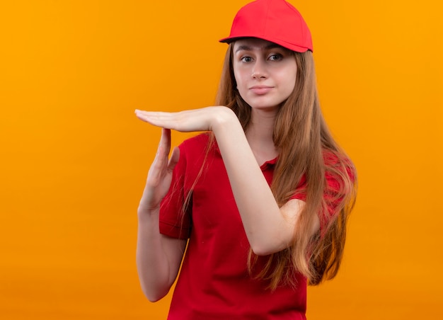 Junges Liefermädchen in der roten Uniform, die Zeitüberschreitungsgeste tut und auf isolierter orange Wand mit Kopienraum