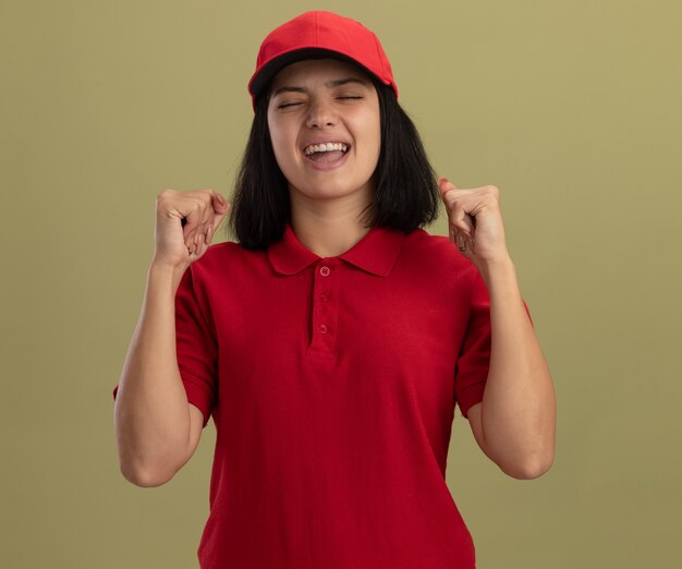 Kostenloses Foto junges liefermädchen in roter uniform und mütze glücklich und aufgeregt geballte fäuste, die über lichtwand stehen