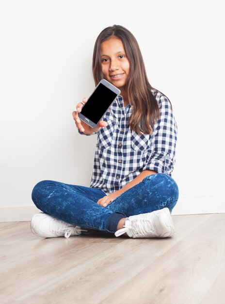 Junges Mädchen auf dem Boden sitzend mit einem Telefon zeigt