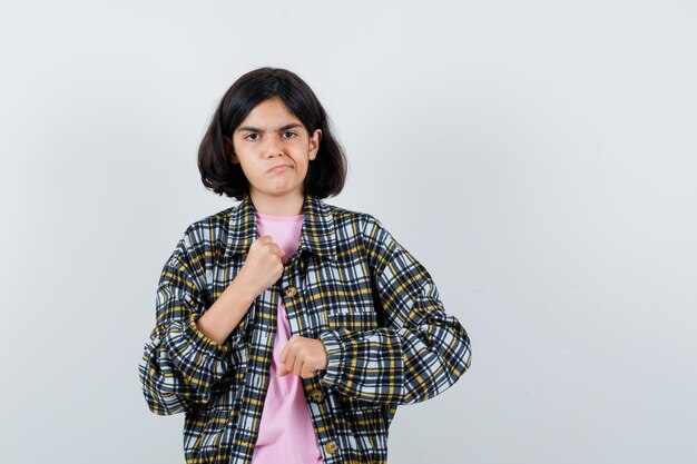 Junges Mädchen ballt die Fäuste in kariertem Hemd und rosa T-Shirt und sieht wütend aus.