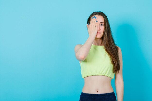 Junges Mädchen bedeckt das halbe Gesicht mit der Hand auf blauem Hintergrund