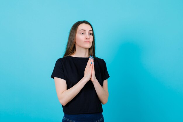 Junges Mädchen betet, indem es die Hände auf blauem Hintergrund zusammenhält