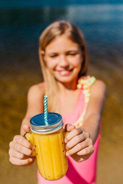 Junges Mädchen bietet Glas mit Saft bei der Stellung auf Strand an