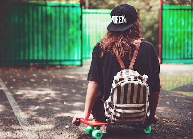 Junges Mädchen, das auf Kunststoff orange Penny Shortboard auf Asphalt in Kappe sitzt