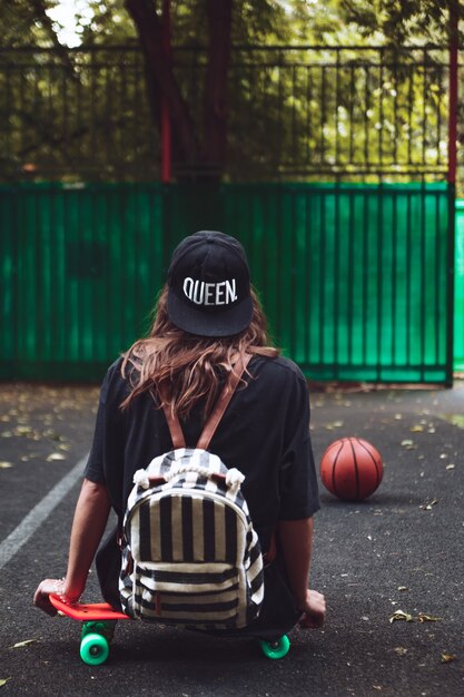 Junges Mädchen, das auf Kunststoff orange Penny Shortboard auf Asphalt in Kappe sitzt