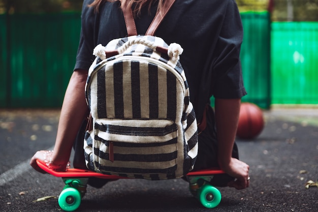 Junges Mädchen, das auf Kunststoff orange Penny Shortboard auf Asphalt in Kappe sitzt