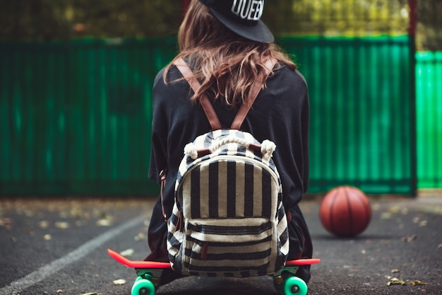 Junges Mädchen, das auf Kunststoff orange Penny Shortboard auf Asphalt in Kappe sitzt