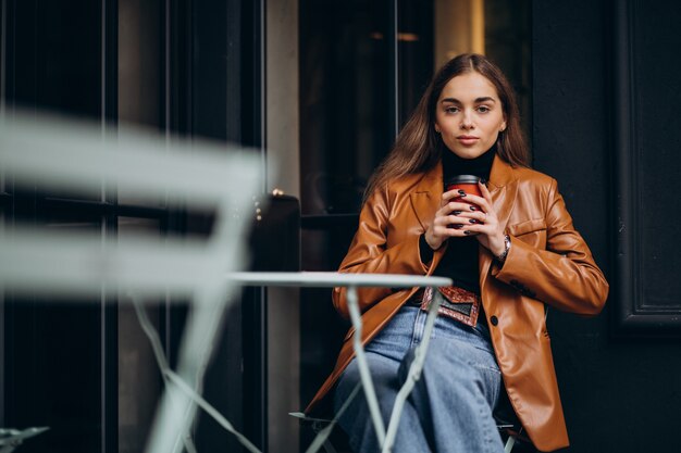 Junges Mädchen, das außerhalb des Cafés sitzt und Kaffee trinkt