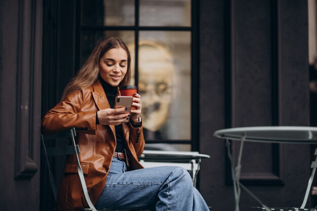 Junges Mädchen, das außerhalb des Cafés sitzt und Kaffee trinkt