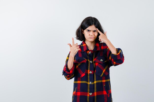 Junges Mädchen, das den Zeigefinger in der Heureka-Geste hebt, während es über etwas in kariertem Hemd nachdenkt und nachdenklich aussieht. Vorderansicht.