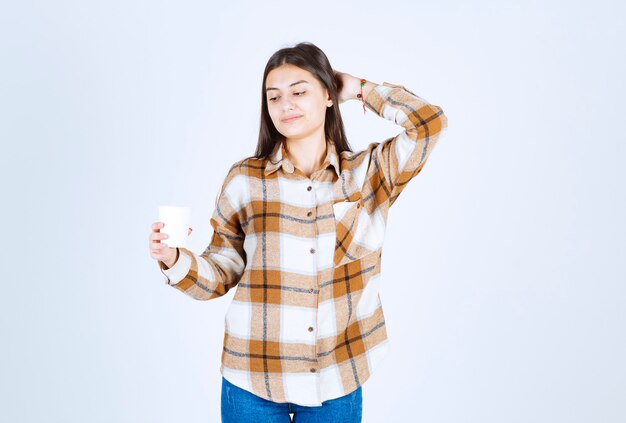 junges Mädchen, das eine Tasse Tee auf der weißen Wand betrachtet.