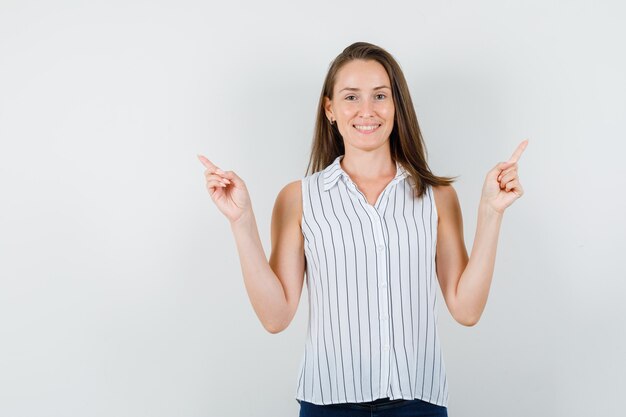 Junges Mädchen, das Finger in T-Shirt, Jeans zeigt und froh aussieht. Vorderansicht.