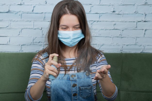 Junges Mädchen, das Gesichtsmaske trägt und Alkohol auf die Hände sprüht