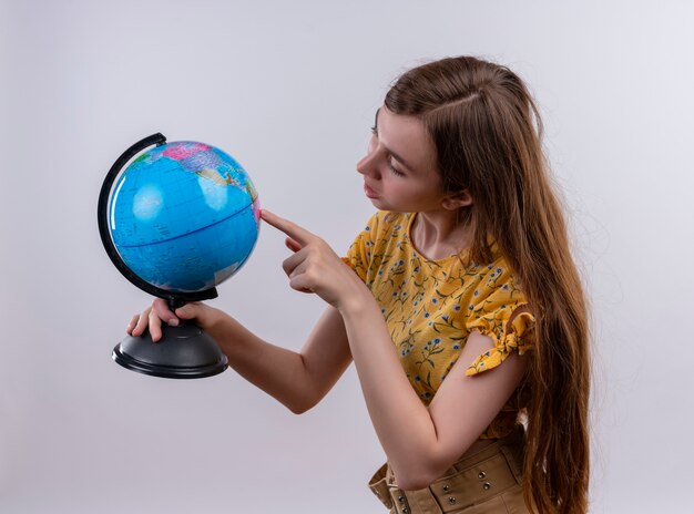 Junges Mädchen, das Globus hält und auf lokalisierte weiße Wand zeigt