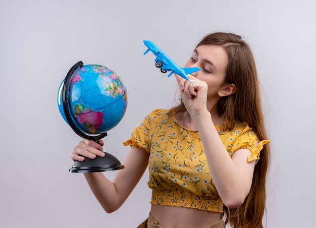 Kostenloses Foto junges mädchen, das globus und modellflugzeug hält und globus auf lokalisierter weißer wand betrachtet