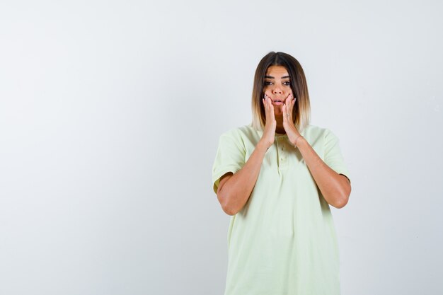 Junges Mädchen, das Hände nahe Mund im T-Shirt hält und überrascht schaut. Vorderansicht.