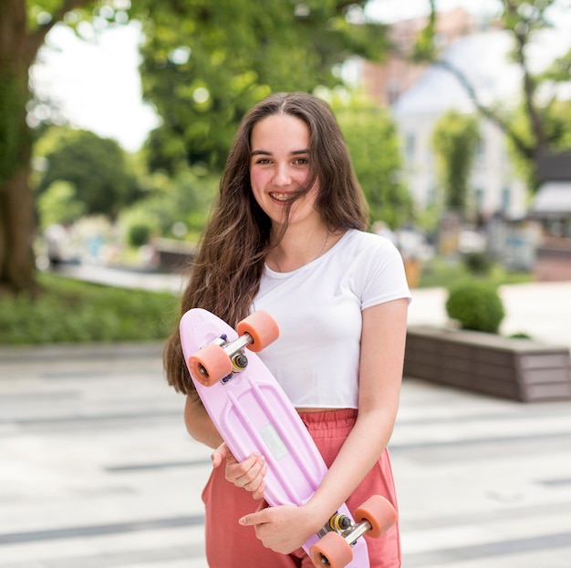 Junges Mädchen, das ihr Skateboard draußen hält