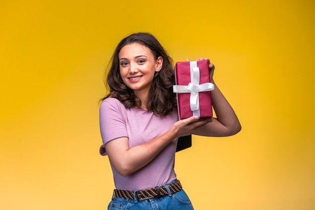 Junges Mädchen, das ihre Geschenkbox auf gelber Wand demonstriert.