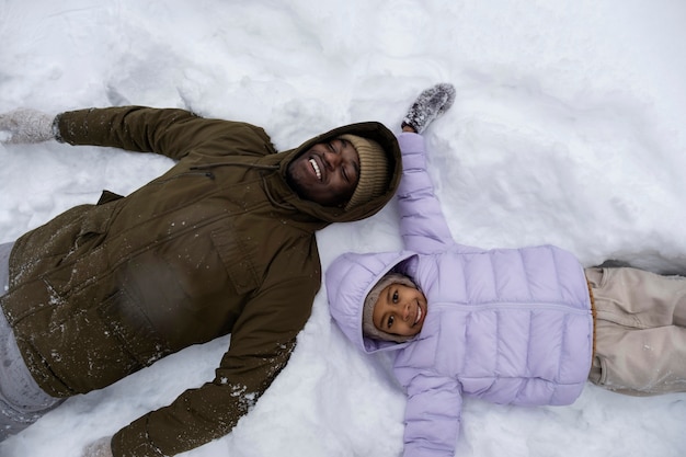 Kostenloses Foto junges mädchen, das im winter mit ihrem vater schneeengel macht