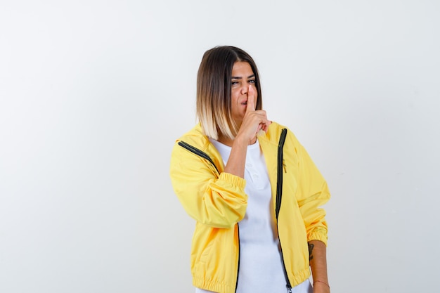 Junges Mädchen, das Stille Geste im weißen T-Shirt, gelbe Jacke zeigt und ernst schaut, Vorderansicht.