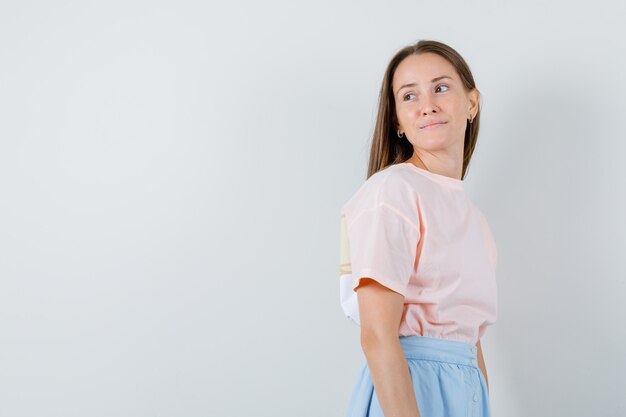 Junges Mädchen, das zurück in T-Shirt, Rock und hoffnungsvoll, Vorderansicht schaut.