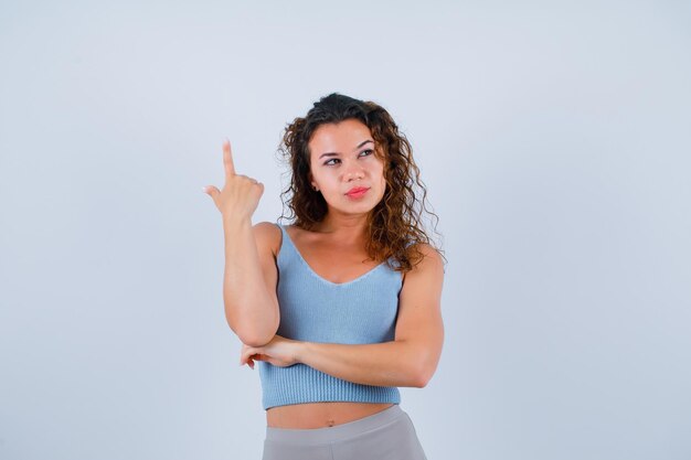 Junges Mädchen denkt nach, indem es mit den Zeigefingern auf weißem Hintergrund nach oben zeigt