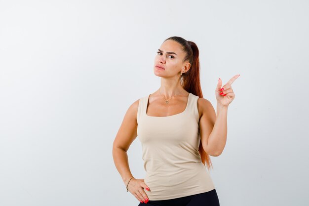 Junges Mädchen im beige Oberteil, schwarze Hose, die mit Zeigefinger nach rechts zeigt