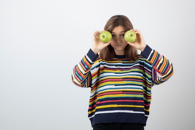 Junges Mädchen im lässigen Outfit, das grüne Äpfel vor Augen hält.