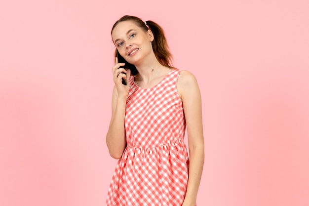 junges Mädchen im niedlichen hellen Kleid, das am Telefon auf rosa spricht