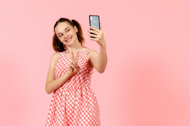 junges Mädchen im niedlichen hellen Kleid, das selfie auf rosa nimmt