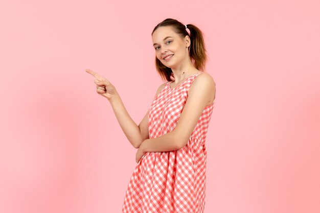 junges Mädchen im niedlichen hellen Kleid mit lächelndem Ausdruck auf rosa